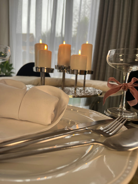 An atmospheric candlelit dinner table setting with pillar candles, accompanied by elegant matte silver cutlery, and adorned with crisp white napkins.